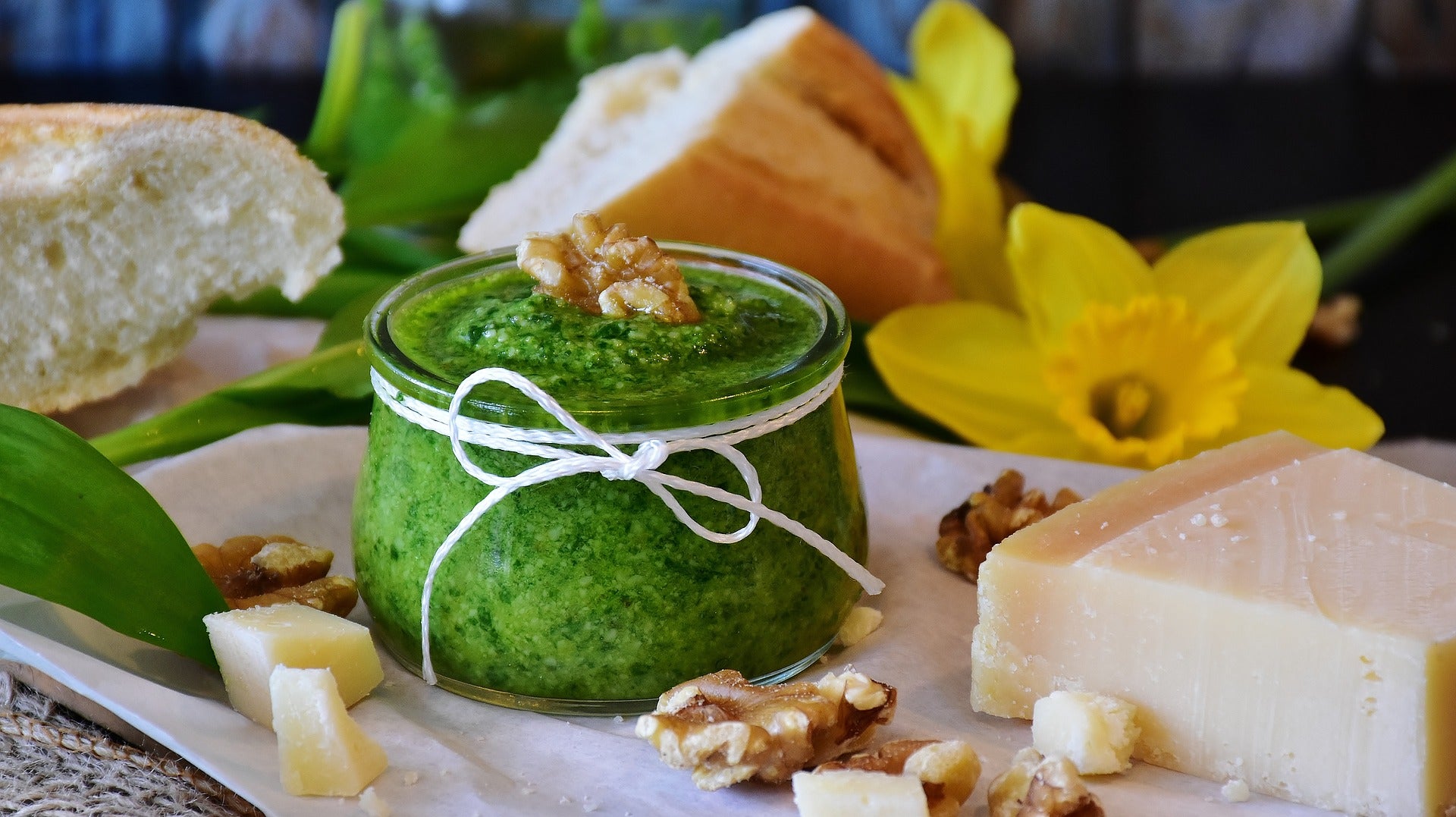 Bärlauchpesto im Glas umrandet von Blüten und Blätter des Bärlauchs